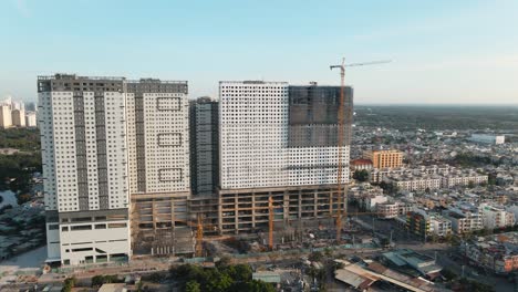 Drone-flying-sideways-shows-a-building-under-construction-with-clear-sky-line-and-residential-area