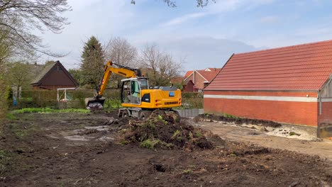 Schwenk-Mit-Arbeitendem-Bagger-Auf-Der-Baustelle-Mit-Gebäuden-Und-Kirche-Im-Hintergrund