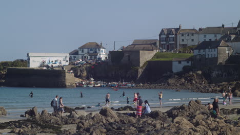 Menschen-Paddeln-Und-Spielen-Am-Strand-Der-Lizard-Halbinsel-Mit-Dem-Hafenbüro-Von-Coverack-Im-Hintergrund