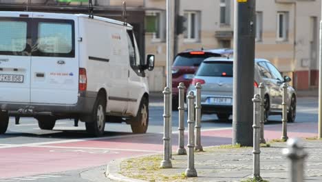 Vehicles-driving-along-a-road-in-Frankfurt-with-people-waiting-for-the-next-bus-in-the-background