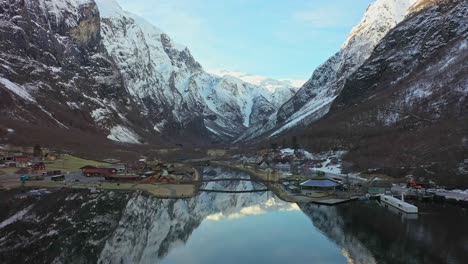 Aéreo-Acercándose-Lentamente-Al-Histórico-Gudvangen-Por-Encima-De-La-Unesco-Escuche-Naeroyfjord---Hermosa-Mañana-De-Invierno-Con-Amanecer-En-El-Fondo-De-La-Montaña-Y-Reflejos-En-La-Superficie-De-Agua-Clara-Y-Crujiente