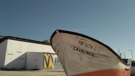 Panning-across-small-wooden-fishing-boats-on-sunny-Costa-de-Caparica-under-blue-sky