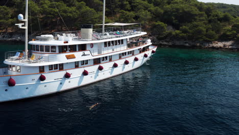 Turista-Nadando-En-El-Océano-Junto-Al-Barco-De-Pasajeros-En-La-Isla-Paklinski,-Hvar,-Croacia