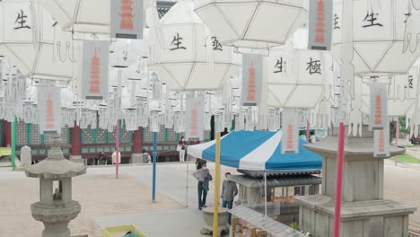 Korean-People-in-Masks-Visit-Bongeunsa-Buddhist-Temple-and-fire-up-candles-in-shrine-worship-place-with-white-lanterns-handing-in-foreground---distant-view