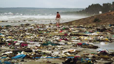 Hombre-En-Topless-Caminando-En-Una-Playa-Sucia-Y-Contaminada-Llena-De-Basura-En-Un-Día-Sombrío