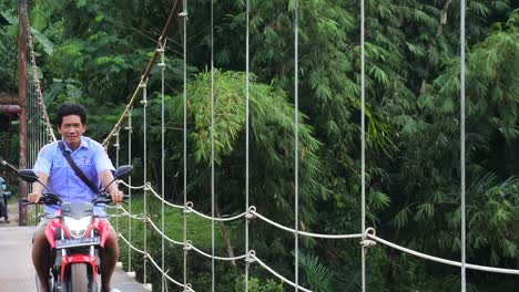 suspension-bridge-over-the-river-with-motorcycle-crossing-on-it-in-the-morning-in-Sukabumi,-west-java,-Indonesia-on-May-4,-2022