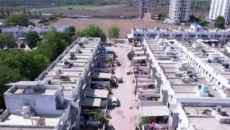 Imágenes-Aéreas-Que-Vuelan-Sobre-Casas-Y-Calles-En-El-Complejo-De-Casas-De-La-Ciudad-De-Rajkot-En-La-Comunidad-India-Rodeada-De-Campos-Verdes-Y-Tejados,-Cielo-Azul-Claro-Día-Soleado