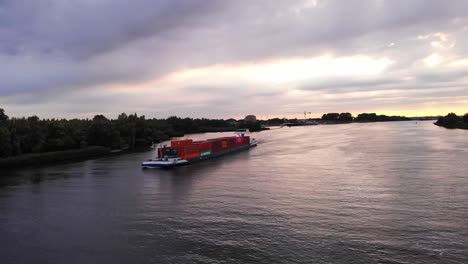 Vista-Aérea-Del-Lado-Del-Puerto-Del-Buque-De-Transporte-De-Contenedores-De-Carga-De-Levante-Navegando-Oude-Maas-Contra-El-Cielo-Del-Atardecer