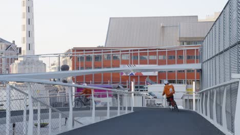 Solo-Come-Comida-Para-Llevar-Jinetes-Con-Traje-Naranja-Andando-En-Bicicleta-Por-El-Puente-Espiral-En-Lovaina,-Bélgica