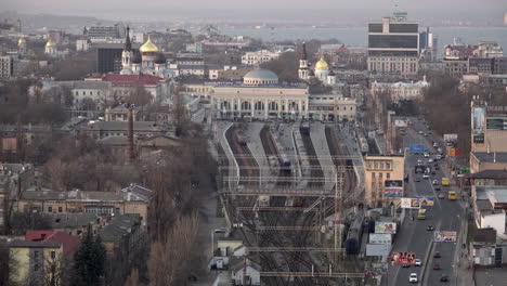 Una-Vista-Aérea-De-La-Ciudad-De-Odesa-Mientras-Un-Tren-Sale-De-La-Estación-De-Tren-Con-Iglesias-Ornamentadas-Y-El-Mar-Negro-Al-Fondo