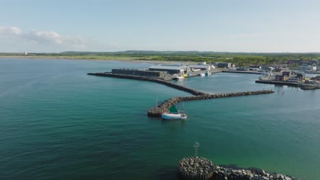 An-aerial-view-A-small-fishing-boat-sails-through-the-harbor-gate-to-the-open-sea-on-a-sunny-evening