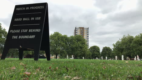 UK-August-2018---A-wooden-sign-warns-the-public-of-a-hard-ball-in-a-boundary-as-a-team-plays-a-game-of-cricket