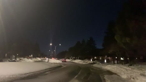 Blick-Vom-Bürgersteig-Auf-Ein-Auto,-Das-Im-Winter-Nachts-Eine-Kurvige-Stadtstraße-Hinunterfährt