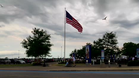 Niña-Discapacitada-Que-Regresa-De-Un-Parque-De-Diversiones-De-Cedar-Point-Después-De-Disfrutar-De-Paseos-Con-Una-Bandera-Americana-En-El-Fondo-Y-Las-Nubes