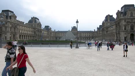 Tourists-walking-in-front-of-the-Louvre-Museum-facade,-in-Paris,-France