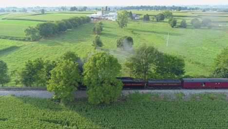 Una-Vista-Aérea-De-Un-Tren-De-Vapor-No-611-Que-Sopla-Humo-A-Través-Del-Campo-Agrícola-En-Un-Día-Soleado-De-Verano-Con-Campos-Verdes