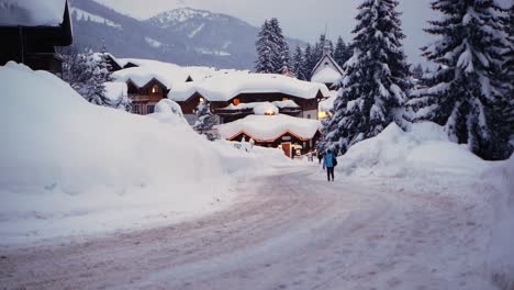 Gente-Caminando-Por-Una-Calle-Cubierta-De-Nieve-En-Un-Pueblo-Durante-La-Hora-Azul-Con-Luces