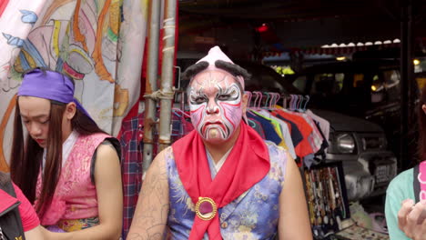 Un-Hombre-Taiwanés-Con-Pintura-Facial-Mastica-Mientras-Mira-A-La-Cámara-Durante-La-Procesión-Taoísta-En-Taiwán---Zoom-In-Shot