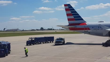 Marshaller-Caminando-Al-Carrito-De-Equipaje,-Aviones-Despegando-En-Segundo-Plano,-Aeropuerto-De-Dallas,-Texas