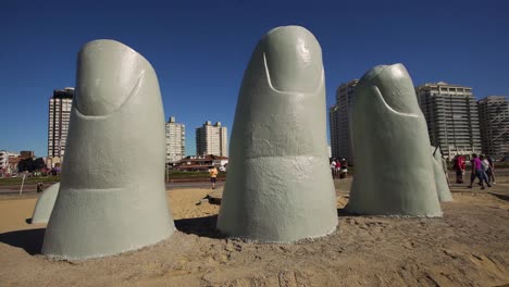 The-Hand-statue-with-tourists-and-city-background