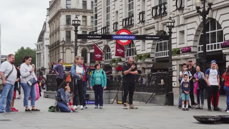 Londoner-U-Bahn-Schild-über-Dem-Eingang-Zur-U-Bahn-Am-Piccadilly-Circus-Square,-Menschen-Stehen-Herum-Und-Beobachten-Straßenaufführungen,-Weitwinkelansicht-Von-Außen