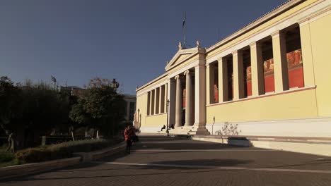 Walking-towards-the-entrance-of-the-University-at-the-Athenian-Trilogy-in-Athens,-Greece,-on-a-gimbal-tracking-shot