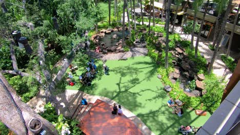 Gente-Sentada-En-El-Parque-Con-Hierba-Verde-Cortada-Y-Palmeras-Disfrutando-Del-Sol-Y-El-Buen-Día