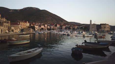 Vista-De-Komiza,-Sus-Numerosos-Barcos-Atracados-En-La-Cala-Y-El-Castillo-Al-Atardecer-Con-Suaves-Olas