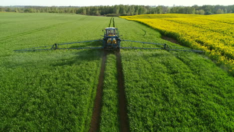 Tractor-Con-Remolque-Y-Brazo-Ancho-De-Metal-Con-Boquillas-Rociando-Pesticidas-Sobre-El-Campo-Verde