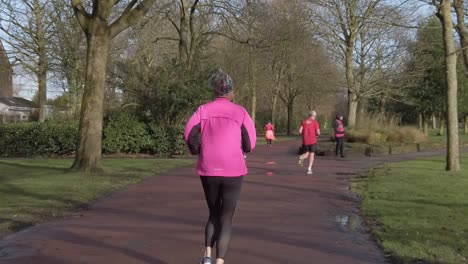 Active-fitness-group-jogging---walking-in-wet-rainy-park-in-slow-motion-rear-tracking-view