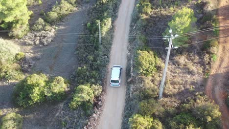 White-van-approaching-Fontainhas-Beach-on-winding-dirt-road,-Aerial-top-view-follow-shot