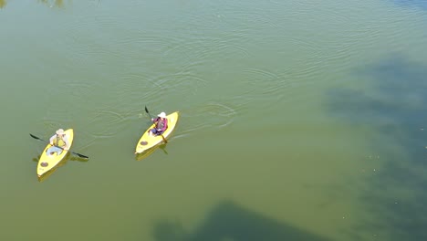 Una-Vista-Aérea-De-Dos-Personas-Navegando-Lentamente-En-Kayak-Desde-La-Parte-Superior-Derecha-A-La-Parte-Inferior-Izquierda-De-La-Pantalla-En-Un-Día-Tranquilo-Y-Soleado