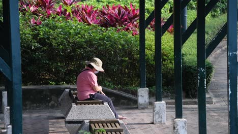 A-woman-sits-at-a-bench-outdoors-while-wearing-a-face-mask-at-a-park-while-social-distancing-still-in-place-due-to-the-Coronavirus-epidemic,-officially-known-as-Covid-19,-in-Hong-Kong