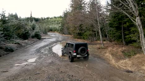 Un-Jeep-Negro-Solitario-Se-Sumerge-En-Un-Charco-De-Lodo-Profundo,-Antena-En-Cámara-Lenta,-Editorial-Ilustrativa