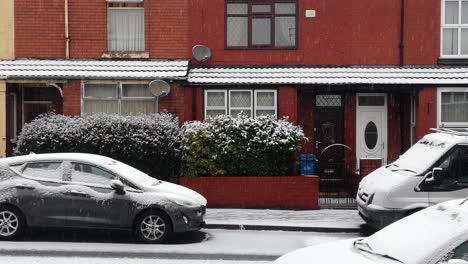 Idyllic-light-winter-snow-falling-in-street-of-town-houses-and-parked-cars