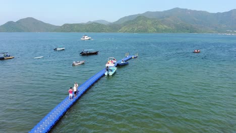 Locals-walking-on-a-small-pier-in-Hong-Kong-with-small-boats-in-the-water-on-a-summer-day