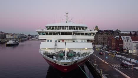 Toma-Aérea-Ascendente-Sobre-La-Proa-Del-Crucero-Hurtigruten-Amarrada-En-El-Puerto-De-Bergen-Al-Anochecer-De-La-Mañana