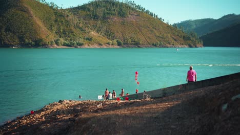 Muelle-Del-Lago-Del-Río-Con-Gente-Nadando,-Bote-Deportivo,-Flotador-Rojo-En-El-Sol-De-Verano-4k