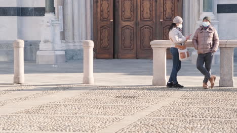 Verlobtes-Paar-Mit-Gesichtsmaske,-Das-Während-Der-Covid-19-Pandemie-An-Einem-Sonnigen-Wintertag-In-Monza,-Norditalien,-Auf-Dem-Stadtplatz-Vor-Dem-Dom-Von-Monza-Steht