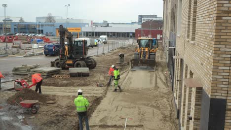 Placing-of-provisional-pavement-stones-time-lapse-with-construction-workers-operating-heavy-machinery-in-preparing-a-sidewalk-in-front-of-newly-build-houses-on-a-drowsy-overcast-day