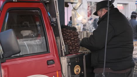 Vendedor-Masculino-Empacando-Castañas-Cocidas-En-Su-Tienda-De-Camiones-Móviles-Durante-El-Invierno