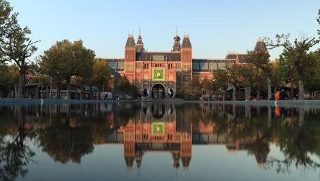 Lapso-De-Tiempo-Al-Atardecer-Del-Museo-De-Arte-En-Amsterdam-Con-Gente-Pasando-Y-La-Escena-Reflejada-En-El-Estanque-De-Agua-En-Primer-Plano