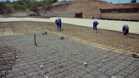 En-Un-Proyecto-Grande,-Los-Hombres-Atan-La-Rejilla-De-Barras-De-Refuerzo-En-Su-Posición-Antes-De-Verter-Los-Cimientos