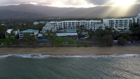 Antena-Sobre-Trinity-Beach-Y-Hotel-Resort-Con-Sol-Atravesando-Las-Nubes