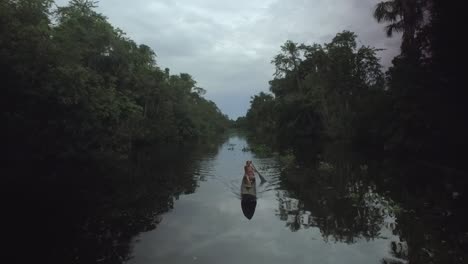 Rising-up-drone-view-of-an-indigenous-person-paddling-a-canoe-in-a-rainforest-river