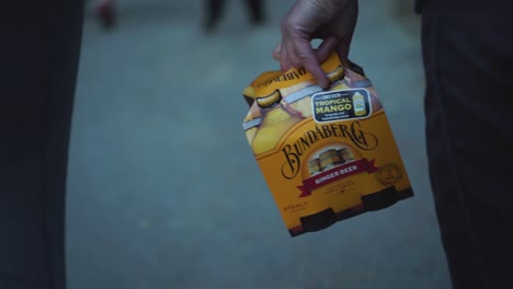 Caucasian-woman-with-blakc-skirt-walking-and-carrying-case-of-Bundaberg-ginger-beer---close-up-from-behind