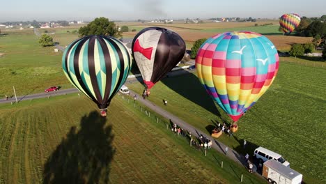 El-Giro-Aéreo-Revela-Coloridos-Globos-Aerostáticos-Que-Aterrizan-En-Una-Pradera,-Los-Pasajeros-Y-Los-Espectadores-Ayudan-A-Desinflar-Los-Globos