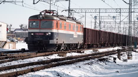 Plano-Medio-Amplio-De-Un-Tren-Eléctrico-Que-Atraviesa-Una-Ciudad-Cubierta-De-Nieve-Durante-El-Día