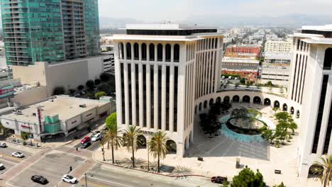 4k-Ariel-perspective-of-a-4-way-crosswalk-with-a-tree-shaded-grassy-area-in-a-city-with-tall-buildings-and-mountains-in-the-background