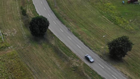 Vista-Aérea-De-Un-Automóvil-Conduciendo-Por-Una-Carretera-Rodeada-De-Campos-Y-árboles